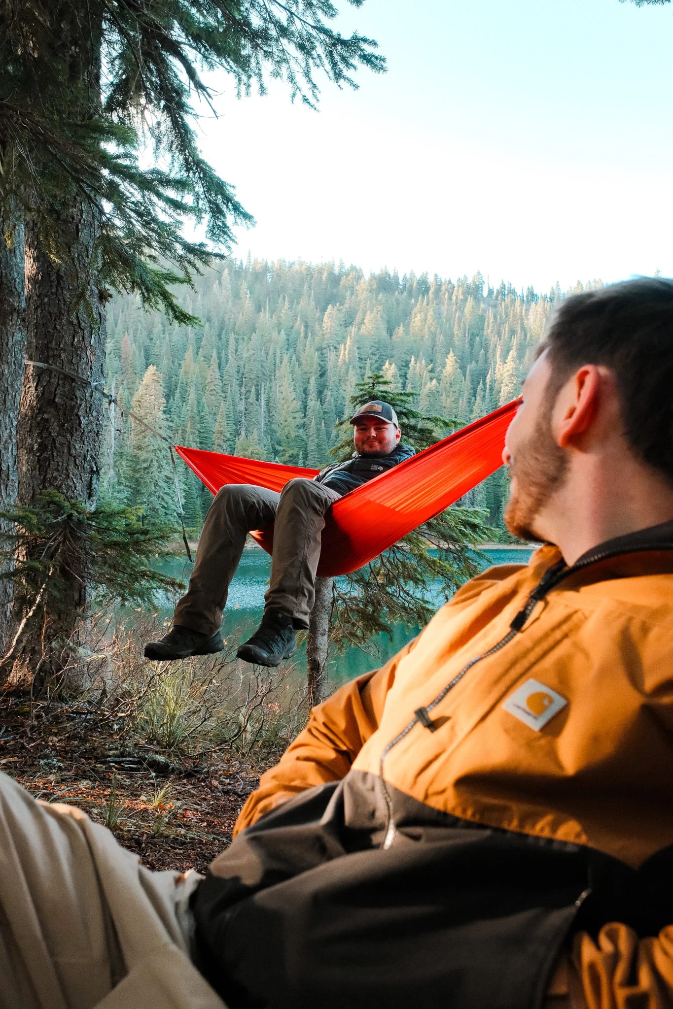 Camper relaxing in a CLIQ chair with a Kammok hammock beside the lake