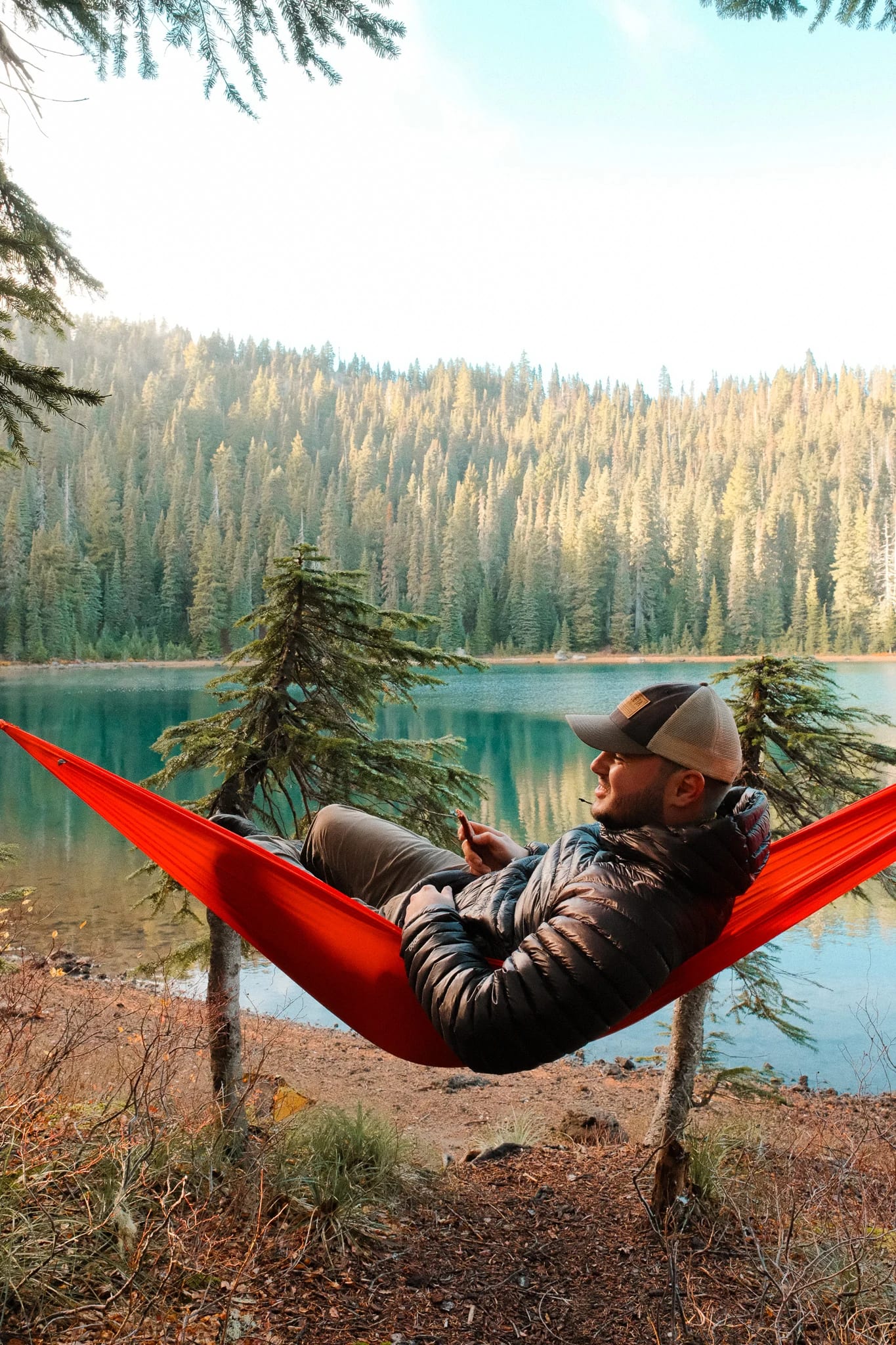 Camper resting in a red Kammok hammock overlooking the lake
