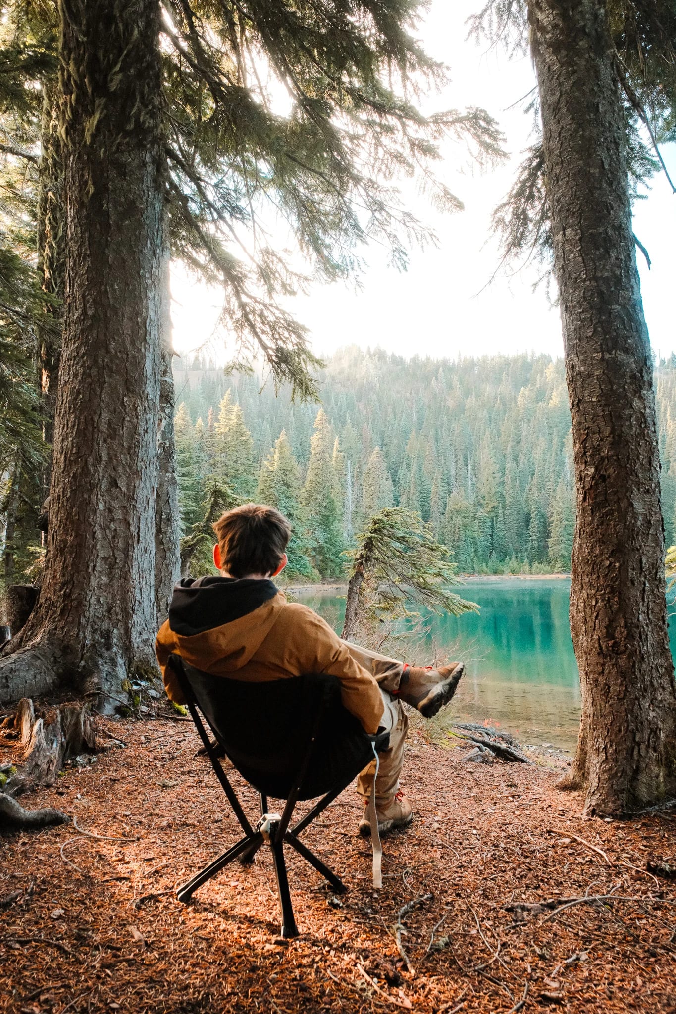 Camper seated in a CLIQ chair beside a forest lake