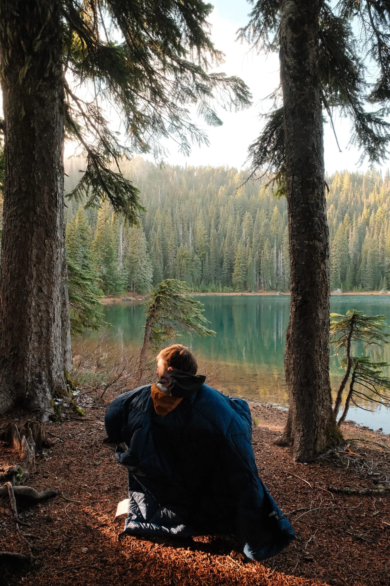 Camper wrapped in a blue blanket beside the lake