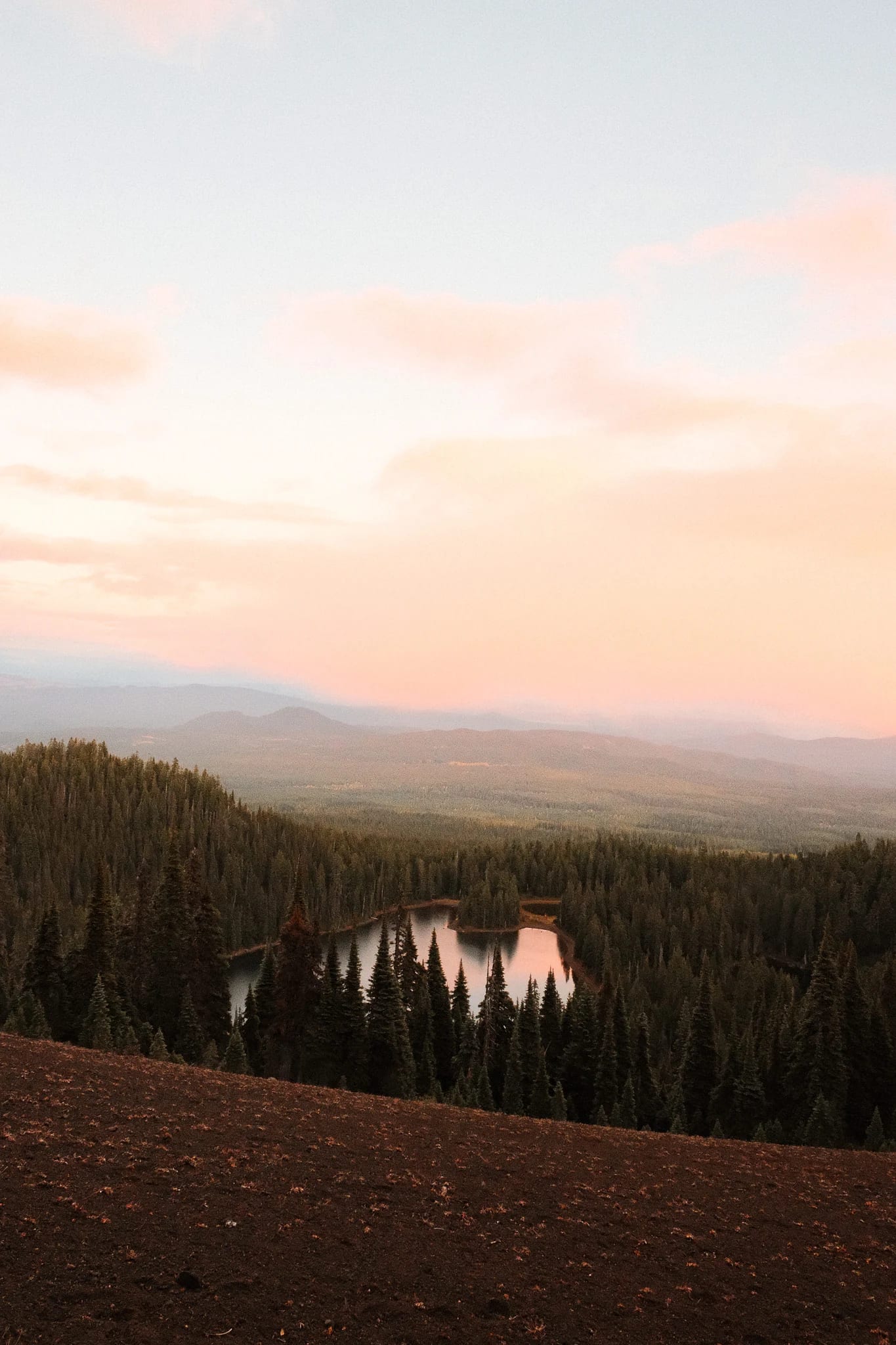 Pastel sunset over distant mountains and a forest lake