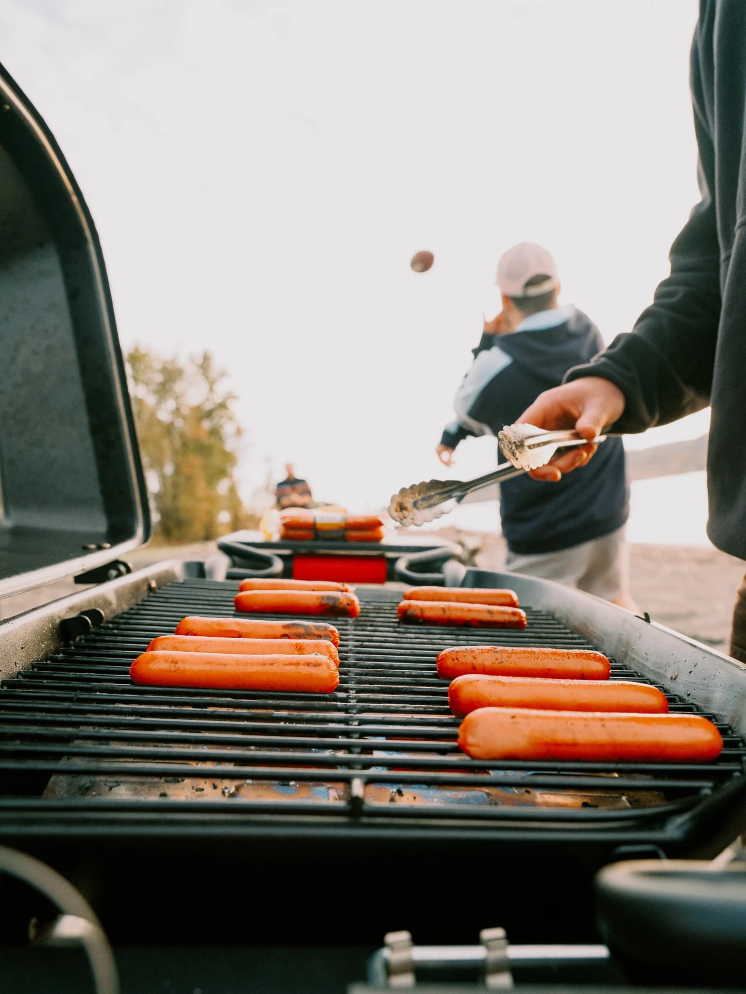 Sausages cook on an open grill at the beach.