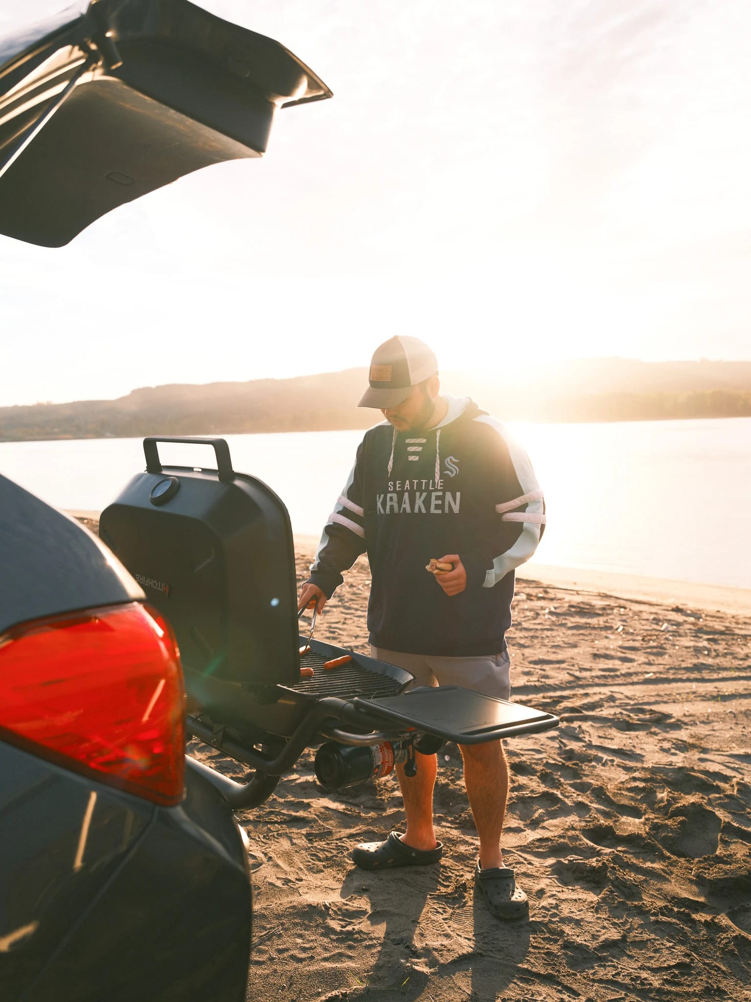 A guest cooks beside a lake in low evening sunlight.