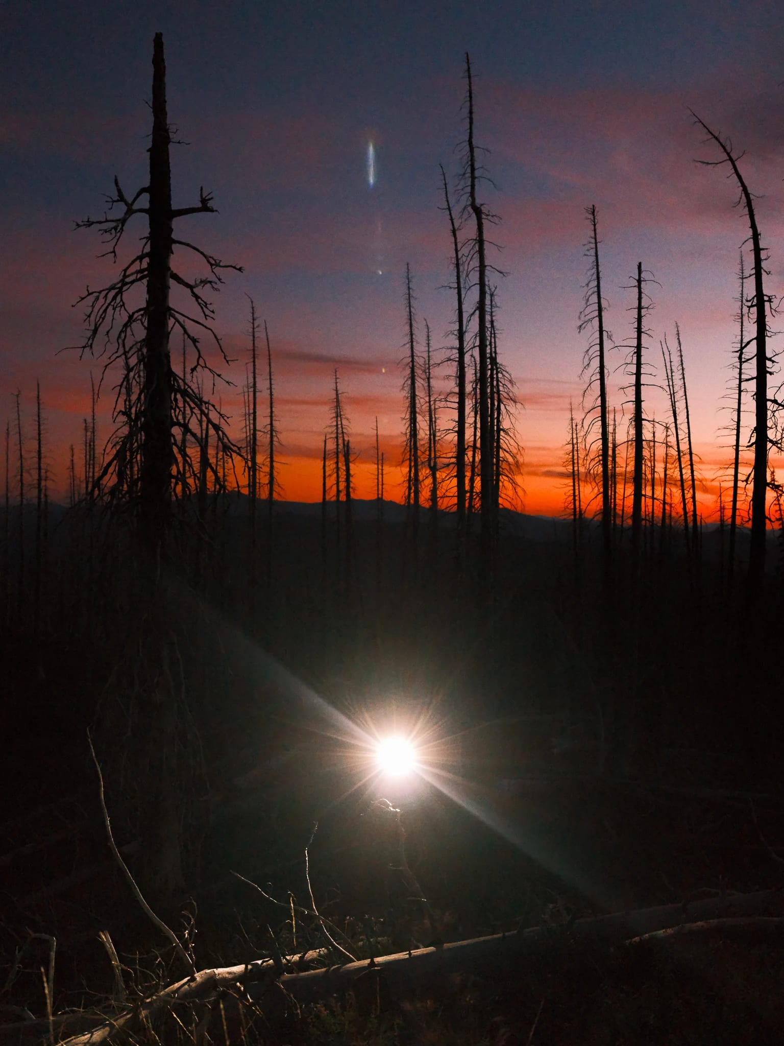 A headlamp shines beneath an orange dawn sky.