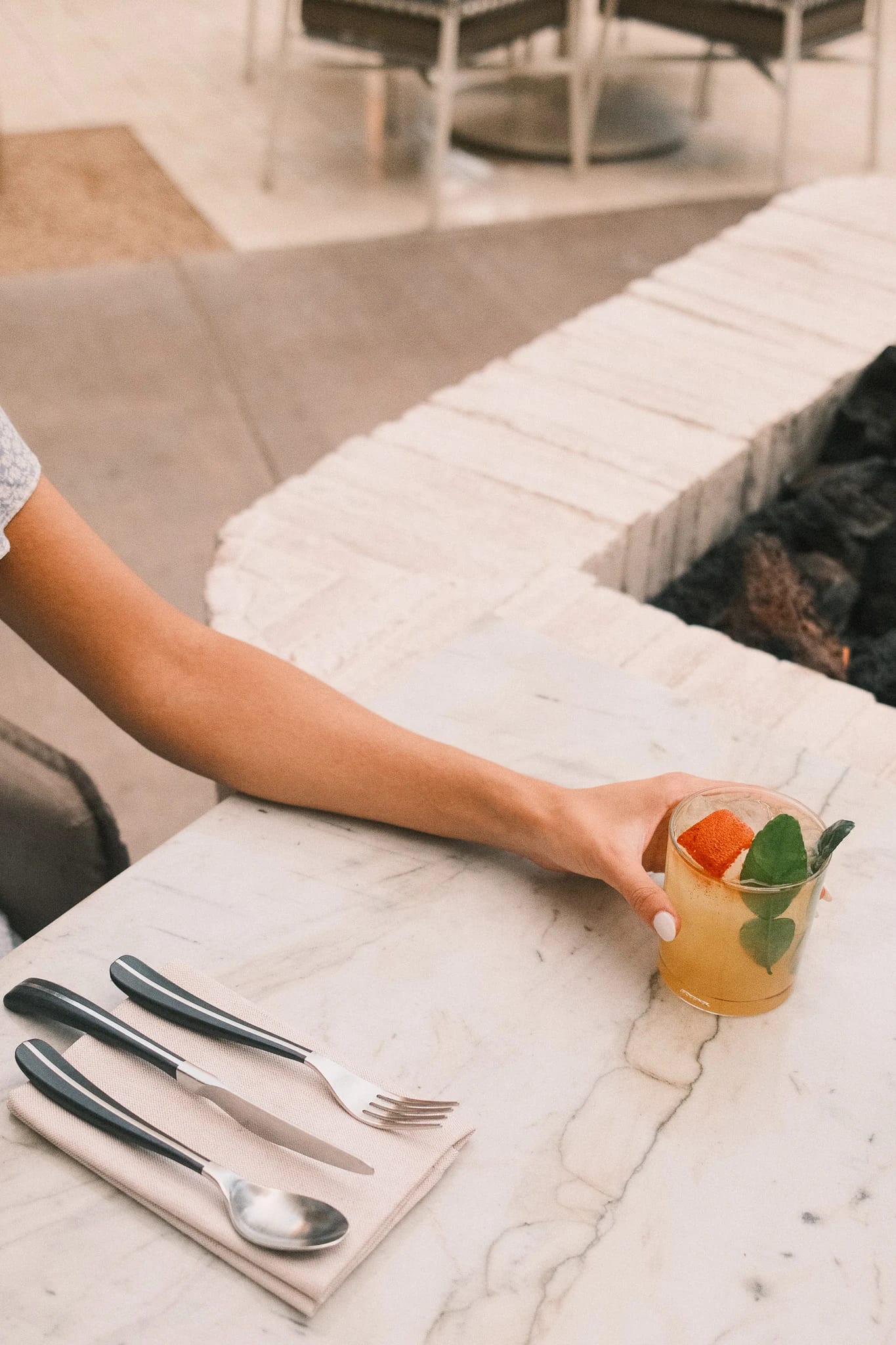 A hand reaches for a cocktail on a marble table.
