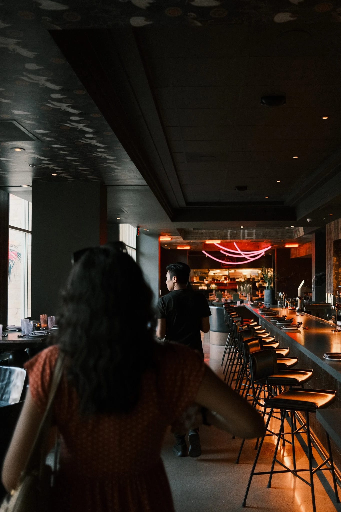 A guest walks toward a warmly lit restaurant bar.