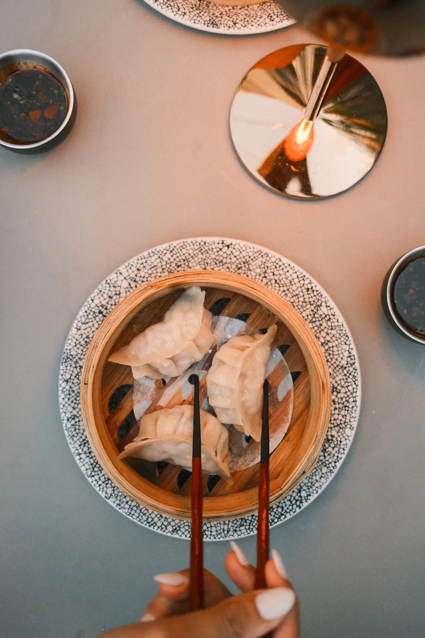 Chopsticks reach for dumplings on a patterned plate.
