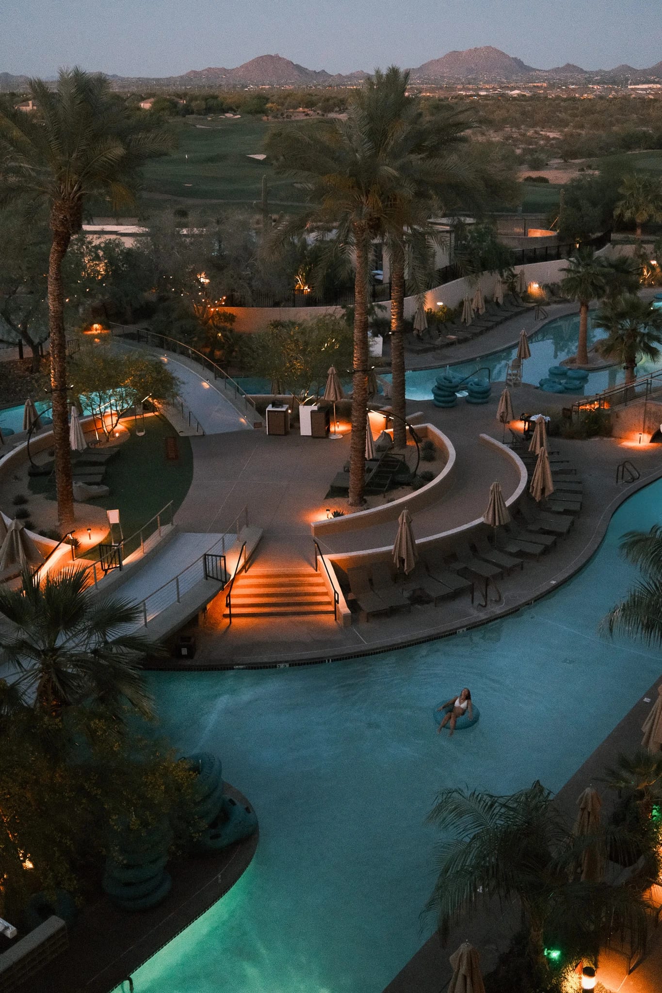 Resort pools glow at dusk beneath desert mountains.