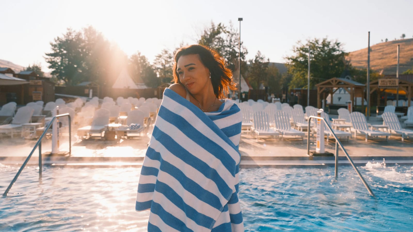 A guest wrapped in a striped towel beside steaming pools at sunrise.