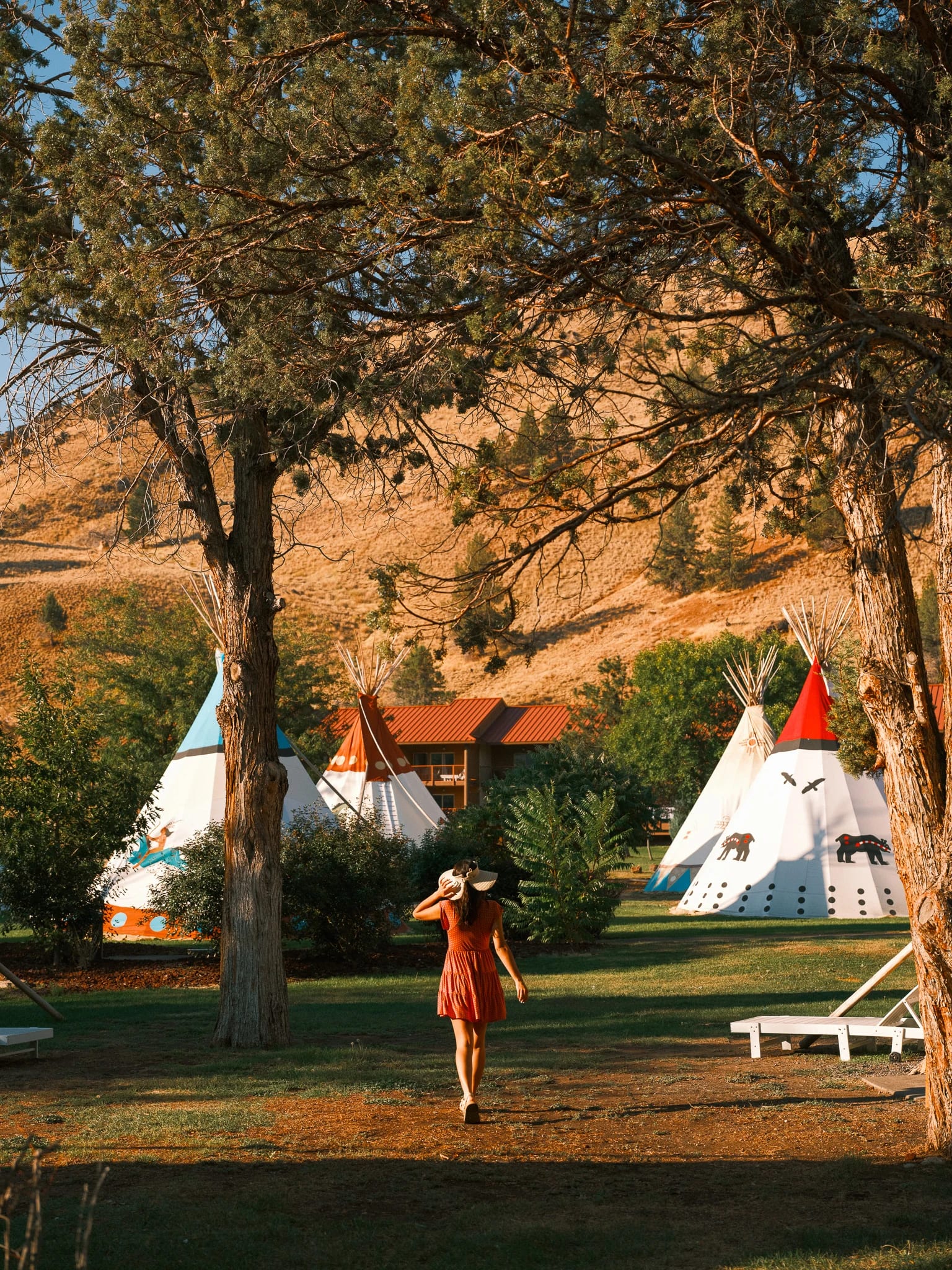 A guest walks between teepees beneath autumn trees.
